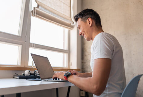 young handsome man in casual outfit sitting at table working on laptop, freelancer at home, view from back